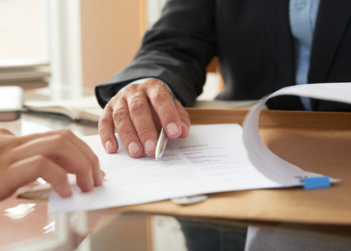 Close-up of businessman examining business contract and signing it at the office desk